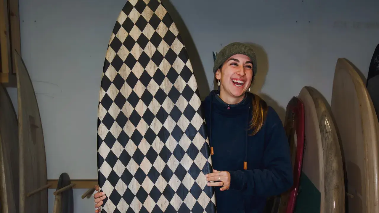 Frau lacht und hält ein selbstgebautes Surfbrett mit Rautenmuster.