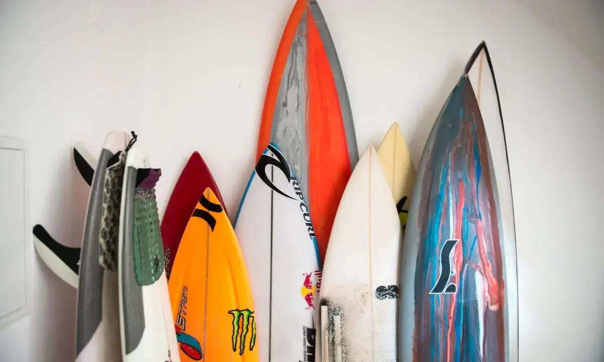 Eine Sammlung bunter Surfbretter steht an einer weißen Wand. Sie sind bereit für das nächste Abenteuer auf den Wellen beim Wellenreiten.