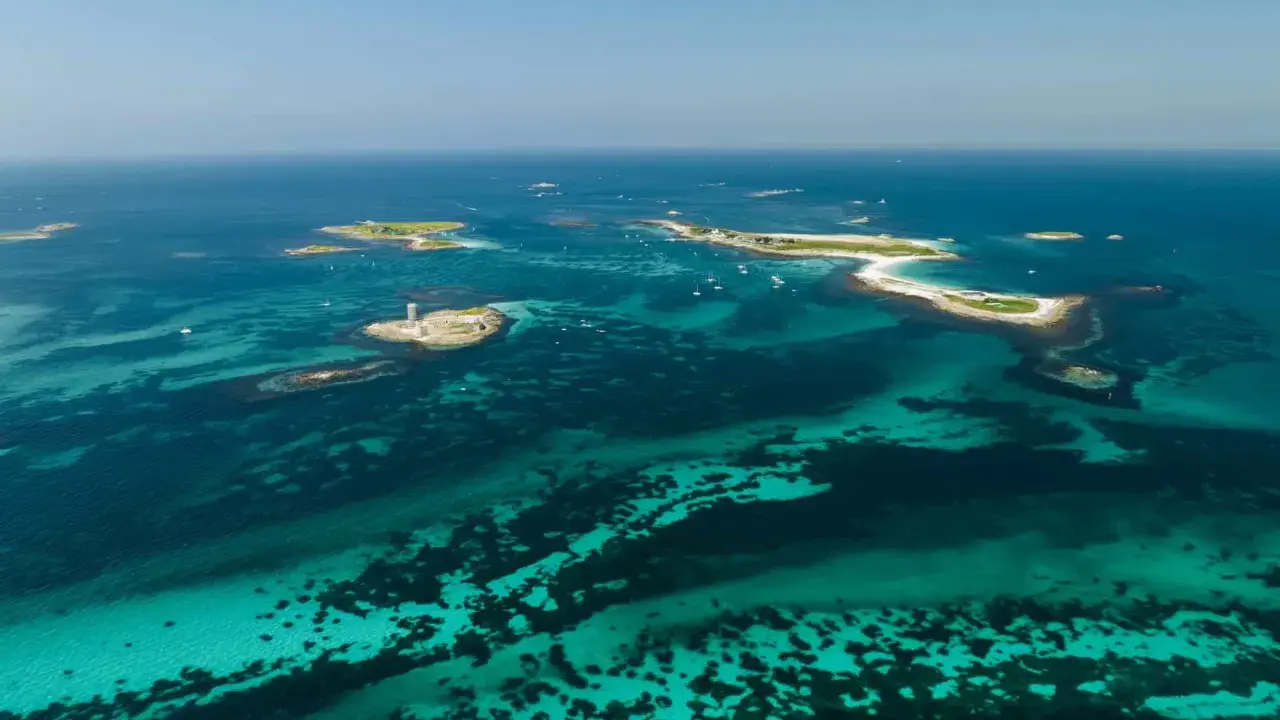 Türkisblaues Wasser umgibt die Glenan Inseln mit einem Leuchtturm auf einer kleinen Insel.
