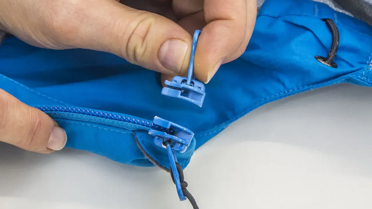 Hände tauschen den blauen Reißverschluss-Zipper an einer Jacke aus.