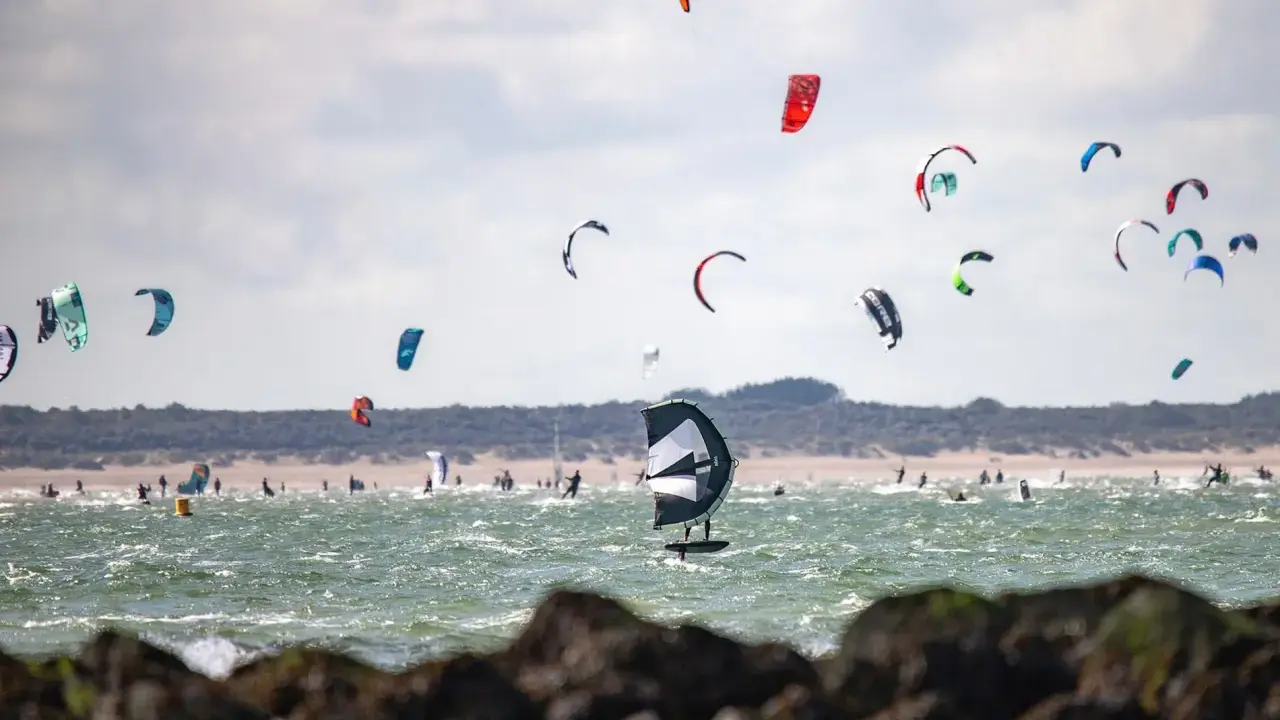 Viele bunte Kites und Surfer bevölkern das Meer am Brouwersdam Zeeland. Ein Kitefoiler schwebt über dem Wasser.