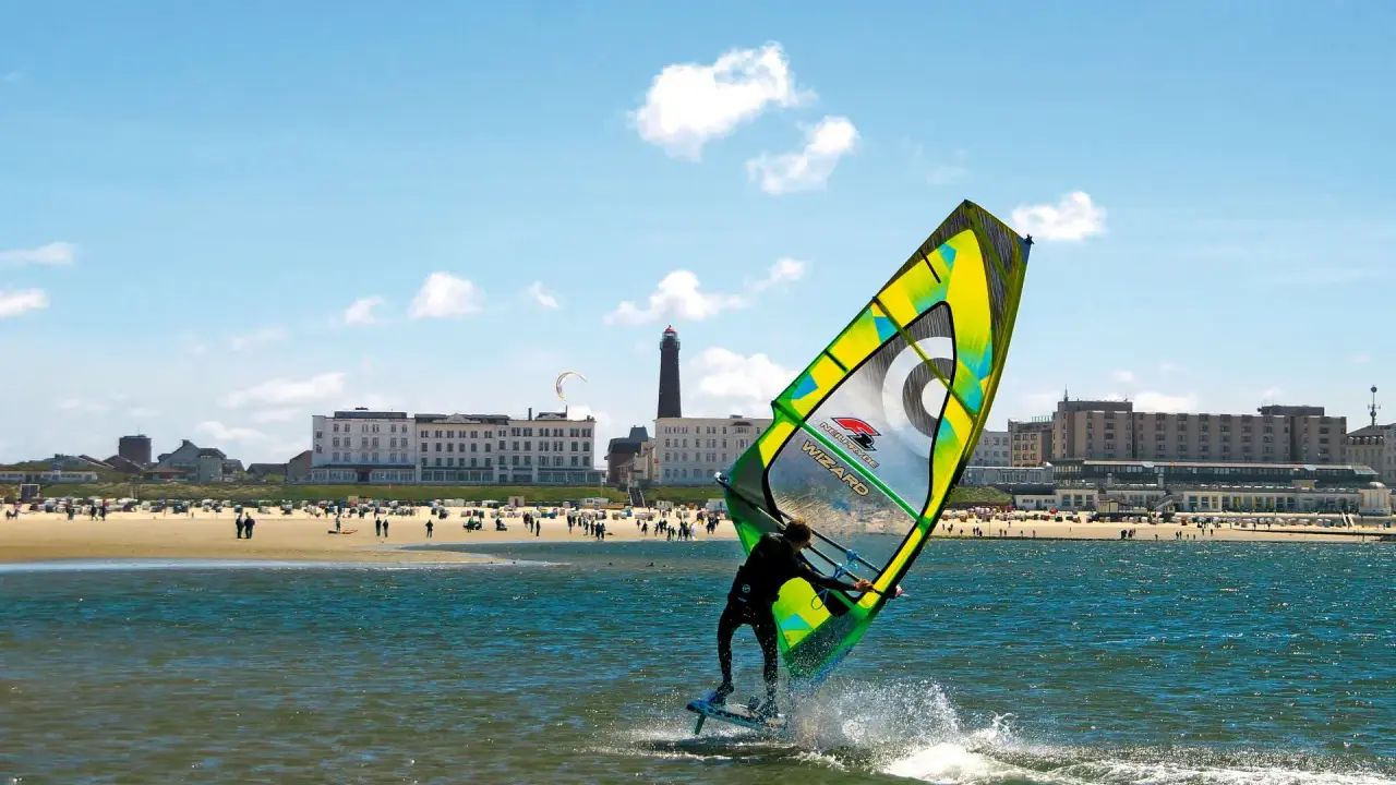Windsurfer auf dem Meer vor Borkum, im Hintergrund der Strand mit Menschen und Hotels.