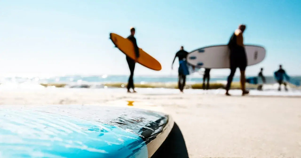 Surfer in Holland tragen ihre Boards zum Wasser. Die Sonne scheint, die Wellen brechen.