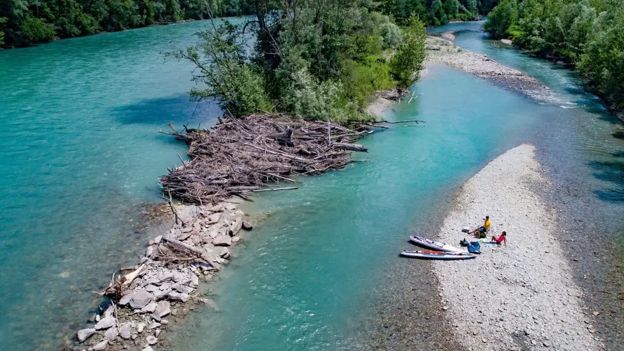 Standup paddling am Feldmarksee: Zwei Personen ruhen sich auf einer Kiesbank aus, während zwei Boards im türkisfarbenen Wasser liegen.