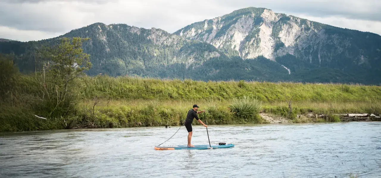Mann auf SUP-Board, der geradeaus fährt, mit Bergen im Hintergrund.