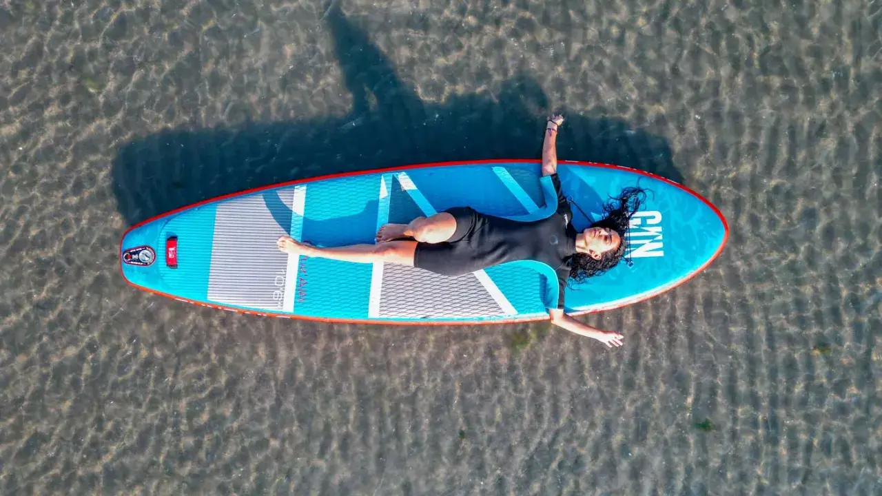 Frauen entspannt auf einem SUP-Board in NRW liegend. Das Board ist blau mit roten Akzenten.