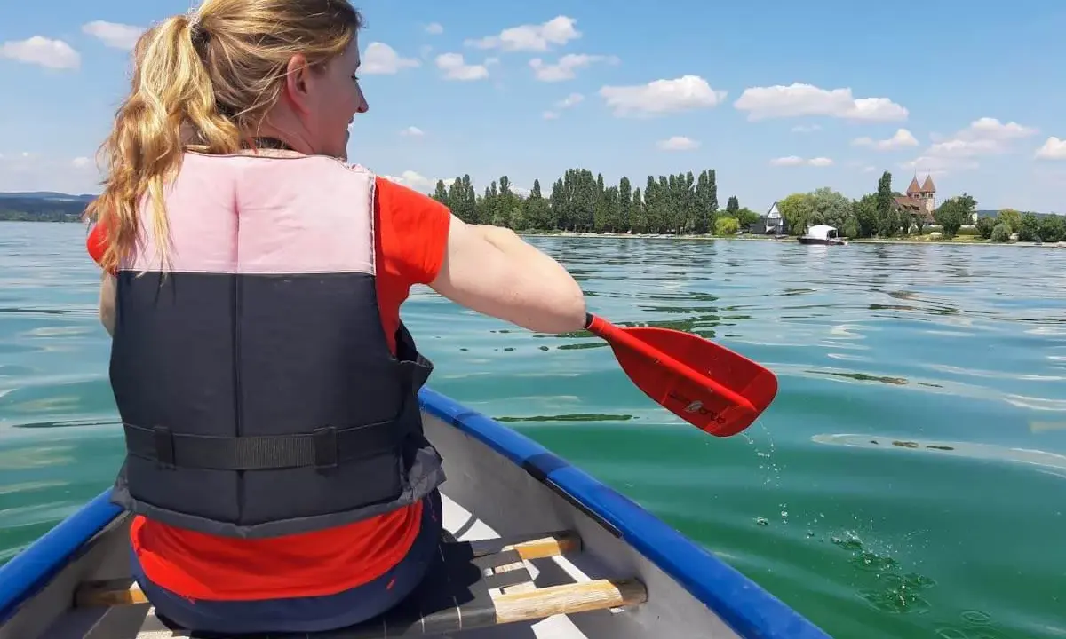 Frau paddelt im Kanu auf einem See, genießt sup touren deutschland. Im Hintergrund: Ufer mit Bäumen und Häusern.