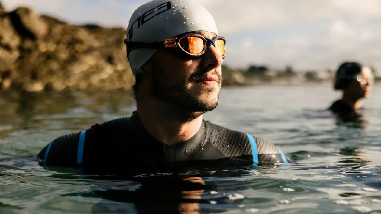 Mann mit Schwimmbrille und Badekappe im Wasser, bereit für das Schwimmen. Die Schwimmbrille reinigen ist wichtig für klare Sicht.