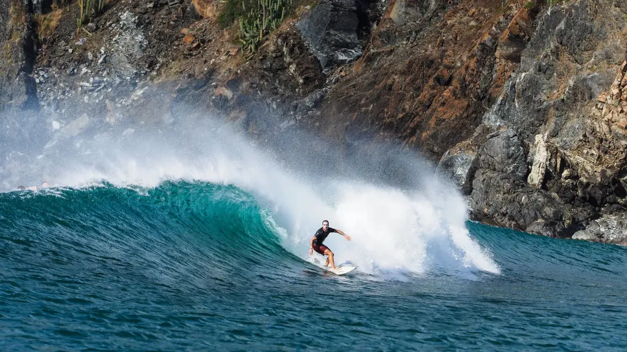 Surfer reitet eine grüne Welle vor einer felsigen Küste. Perfekt für die Surf-App, um die nächste Session zu planen.