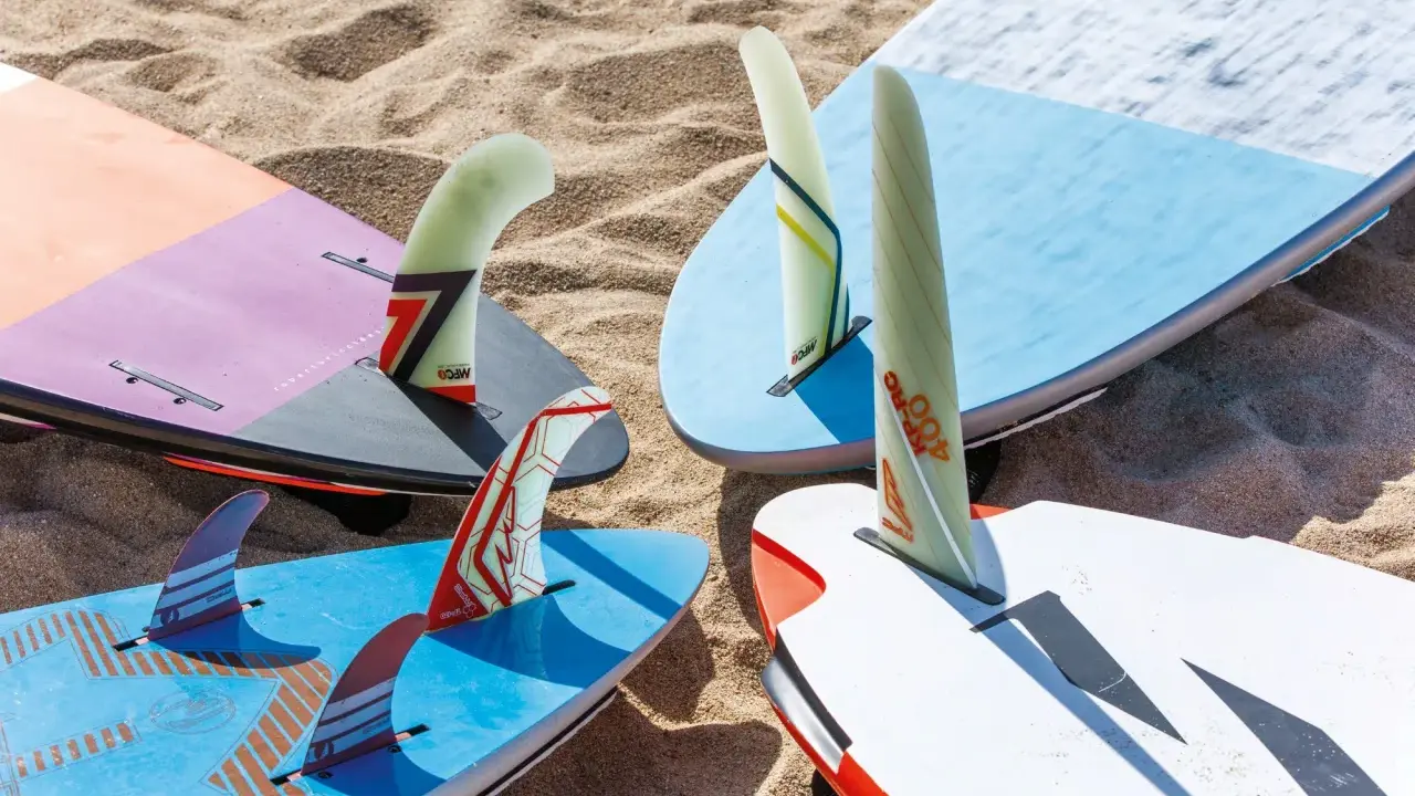 Mehrere Windsurfboards mit bunten Finnen liegen im Sand. Perfekt, wenn Sie ein Windsurfboard kaufen möchten.