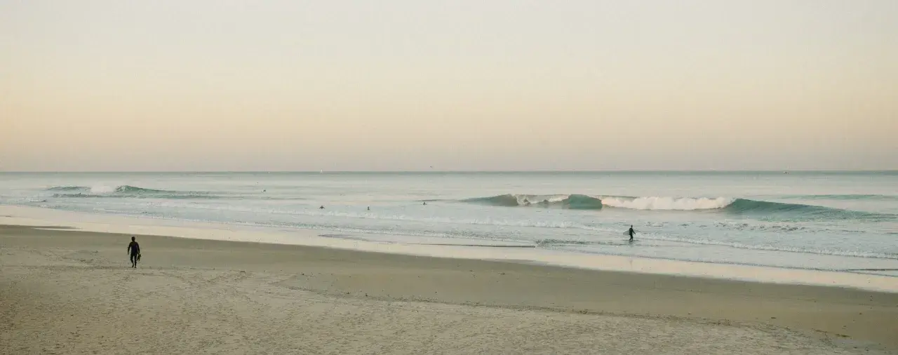 Ein Surfer geht ins Meer, um Cornwall zu surfen. Sanfte Wellen brechen am Strand.