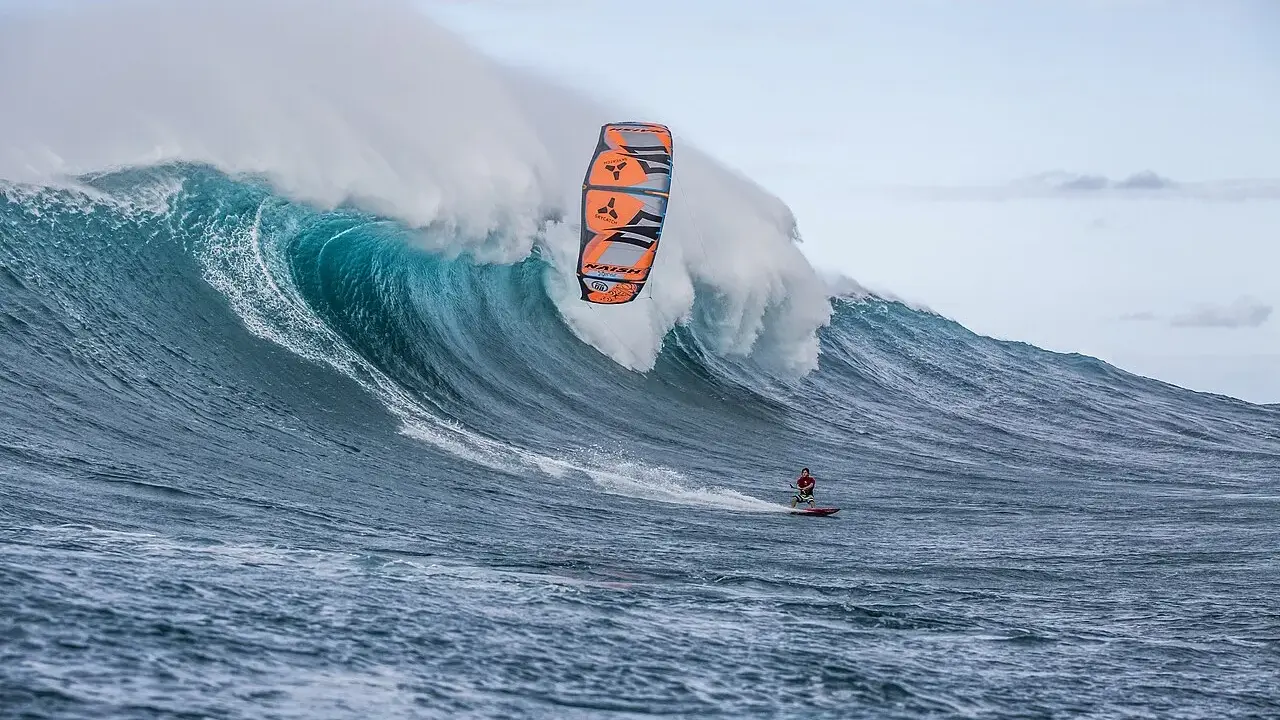 Ein Kitesurfer reitet eine riesige Welle bei Jaws, Hawaii. Die Welle bricht mit gewaltiger Kraft, während der Surfer mit seinem Kite in der Luft schwebt.