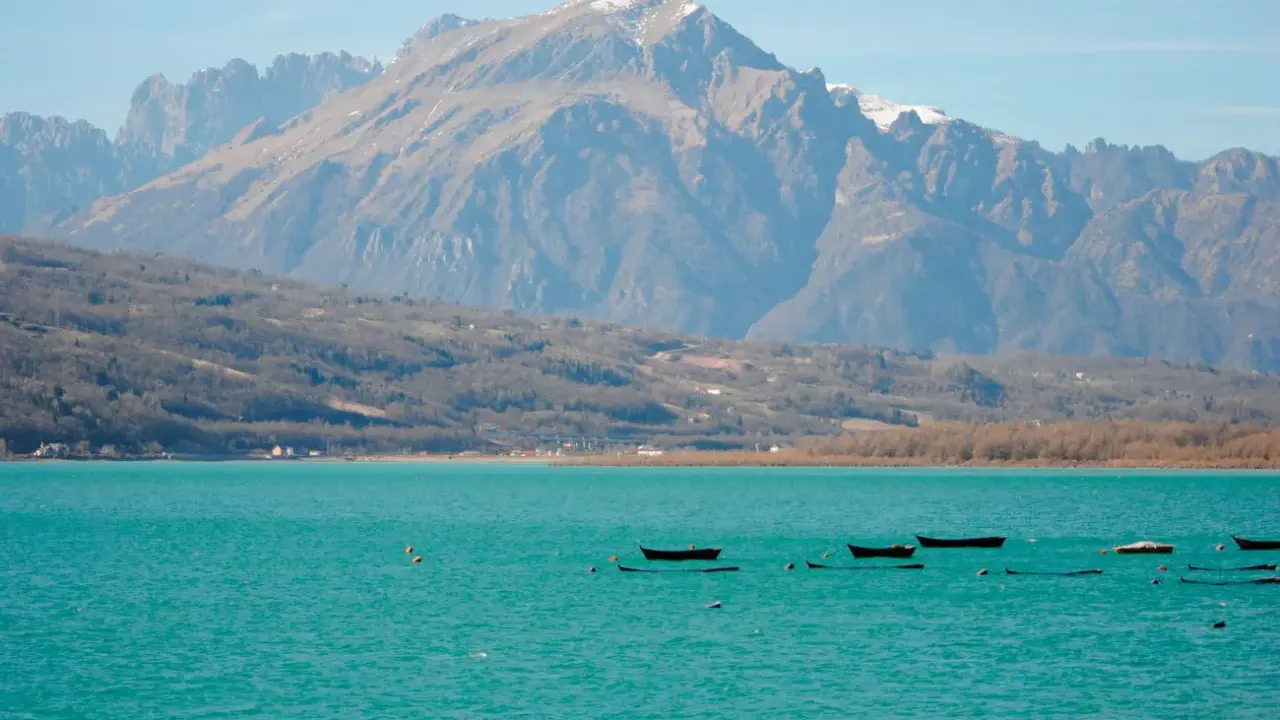 Boote treiben auf dem türkisfarbenen Lago di Santa Croce vor einer majestätischen Bergkulisse.