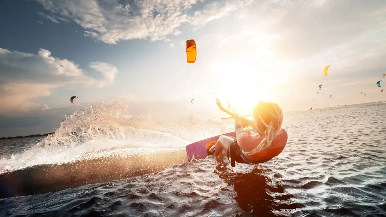 Kitesurferin genießt das Rhodos Surfen im goldenen Abendlicht, spritzt Wasser auf.