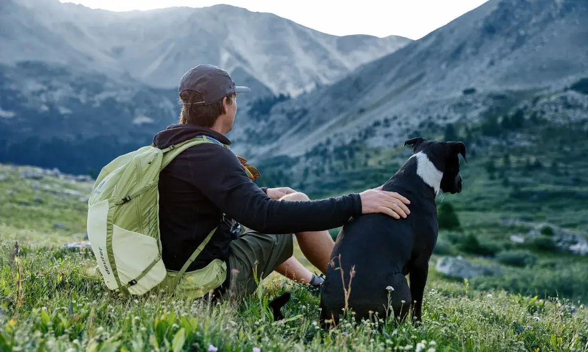 Mann mit Hund und Rucksack in den Bergen. Nach einer Wanderung ist der Rucksack reinigen eine gute Idee, bevor es weitergeht.