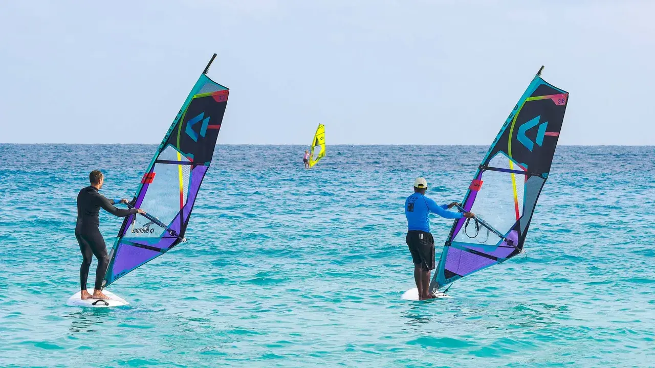 Windsurfer auf dem Meer vor Santa Maria Sal. Zwei Surfer mit bunten Segeln genießen den Tag auf dem türkisfarbenen Wasser.
