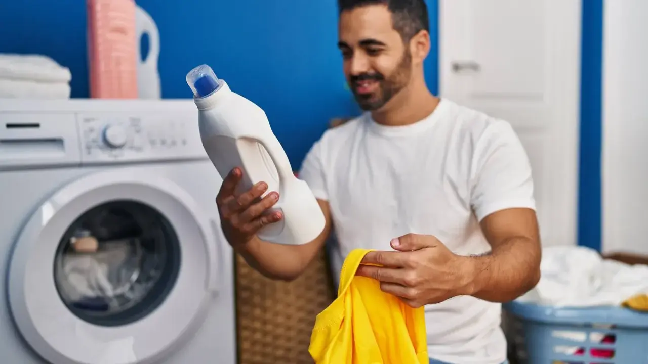 Mann hält Waschmittel und gelbes Trikot bereit, um die Wäsche zu waschen.