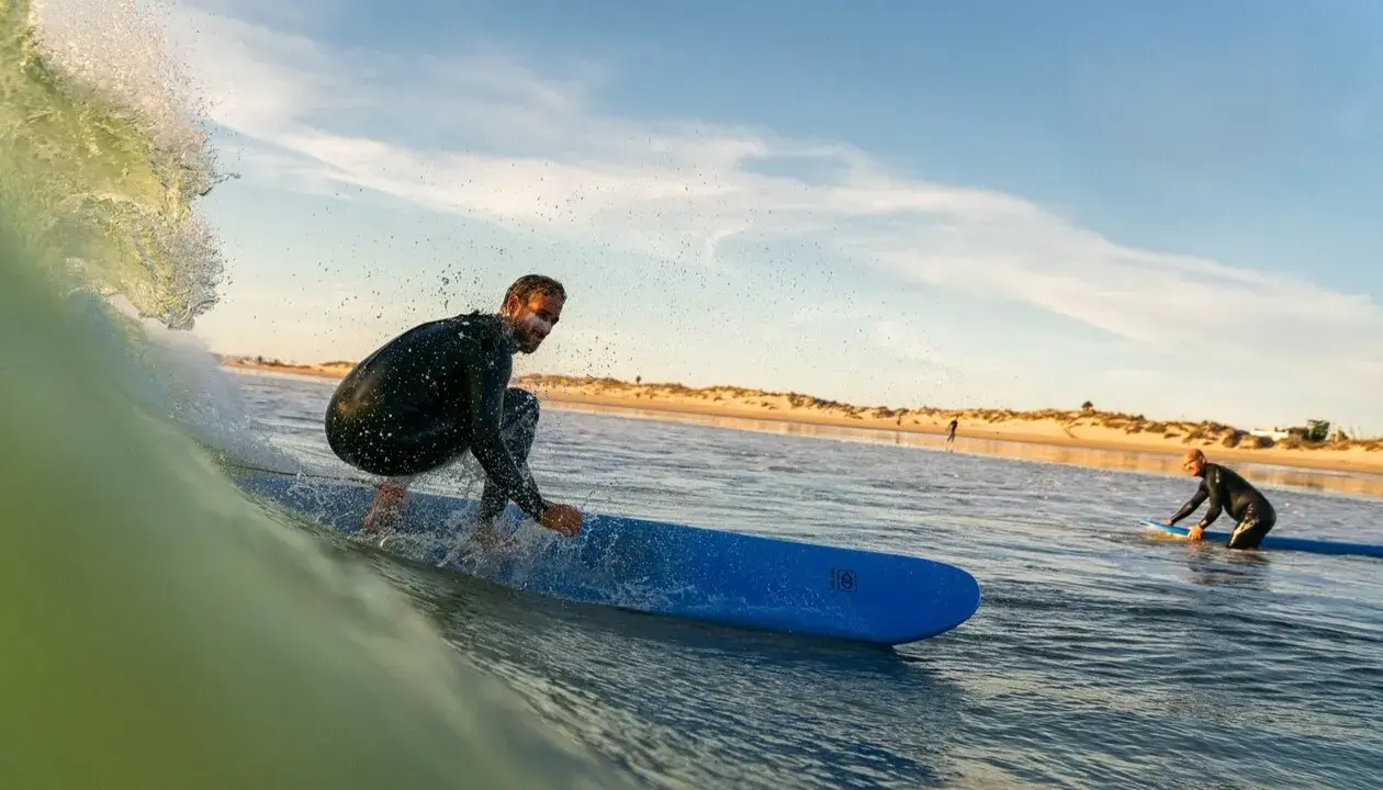 Surfer reitet eine Welle vor der Küste von Tarifa. Ein weiterer Surfer wartet im Wasser.