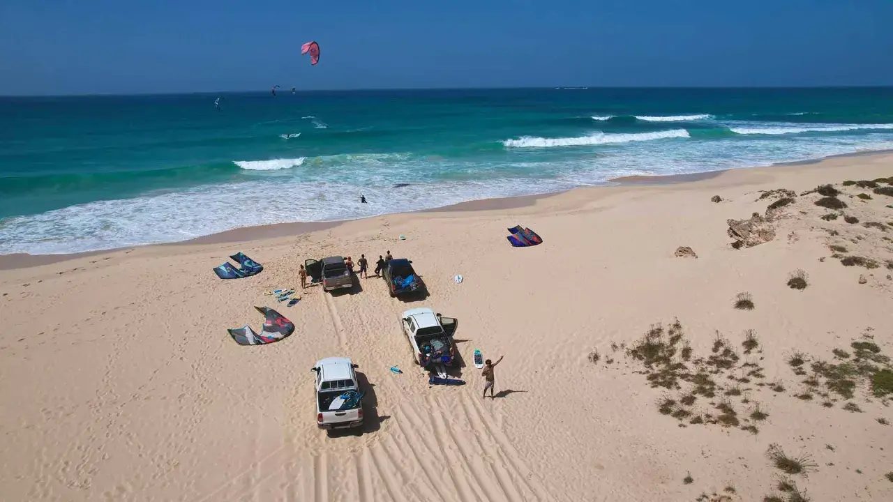 Kitesurfer bereiten sich auf das Windsurfen auf den Kapverden vor. Mehrere Kites liegen am Strand neben Autos.