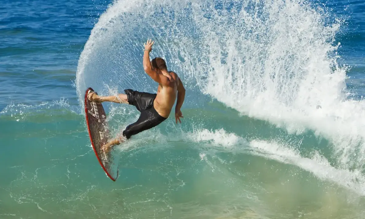 Mann surft ohne segel auf einer welle, die Gischt spritzt. Ein aufregender Moment des Wassersports.