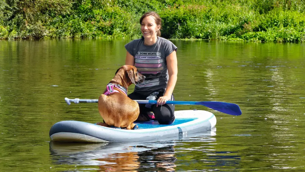 Frau und ihr sup hund krallen auf dem Fluss.