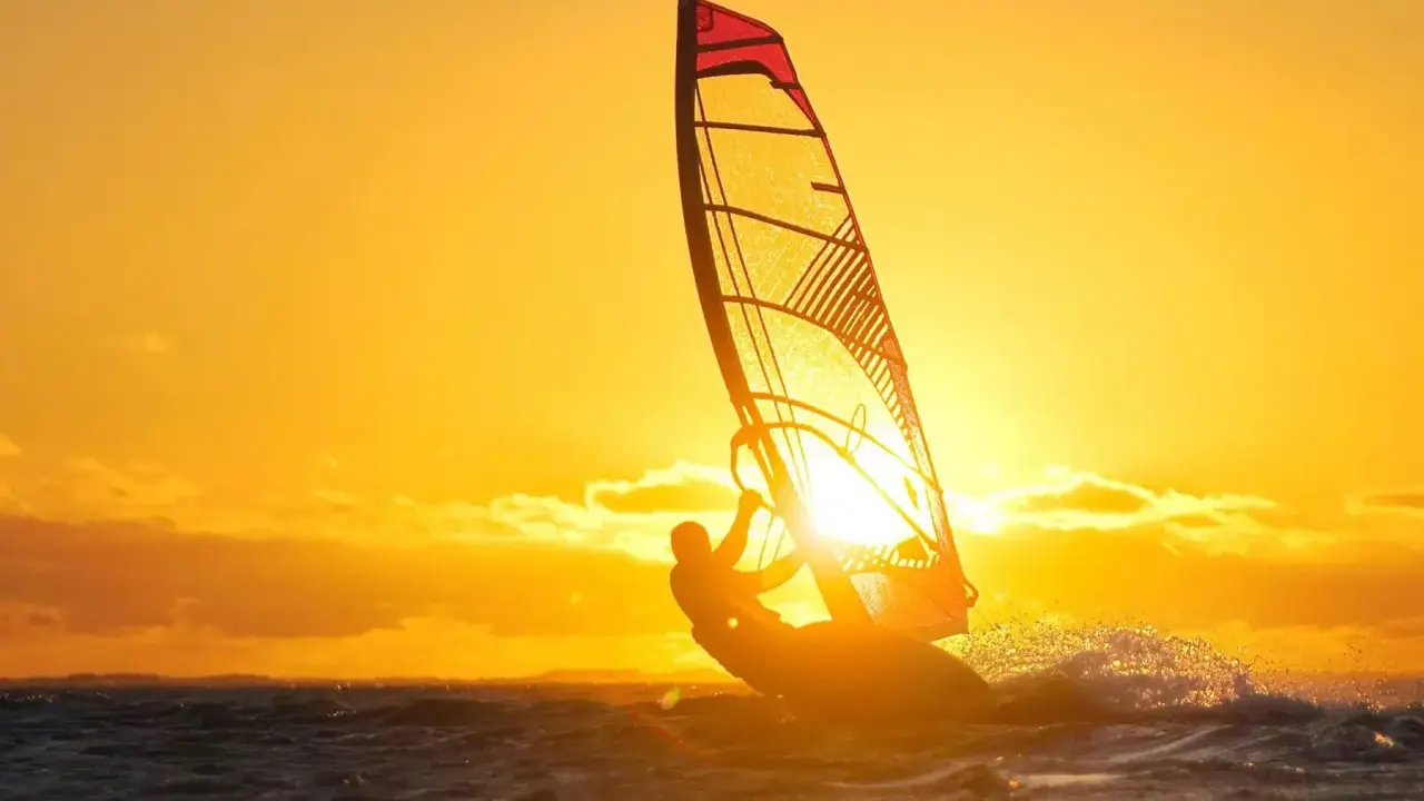 Ein Windsurfer genießt die untergehende Sonne am Ammersee. Das goldene Licht taucht die Szene in warme Farben.