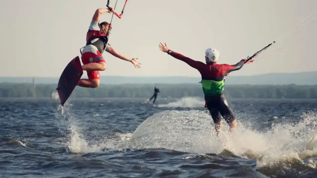 Zwei Kitesurfer springen und reichen sich die Hände auf dem Steinhuder Meer. Ein weiterer Surfer im Hintergrund.