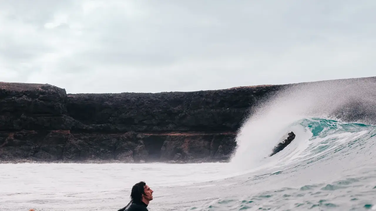 Surfer wartet auf die perfekte Welle vor einer Felswand, um Costa Calma surfen zu gehen.