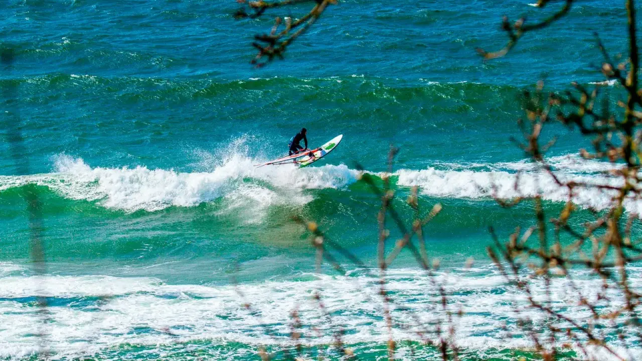 Windsurfer auf einer Welle vor Bornholm. Das türkisfarbene Meer und die Gischt erzeugen ein dynamisches Bild vom Surfen.