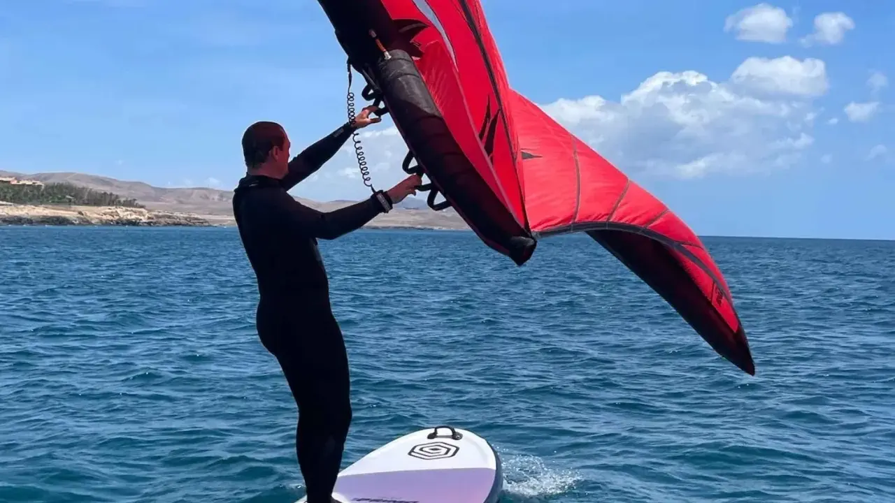 Mann mit rotem Wingboard auf dem Wasser vor Costa Calma. Perfekter Tag für Wassersport am Ion Club.