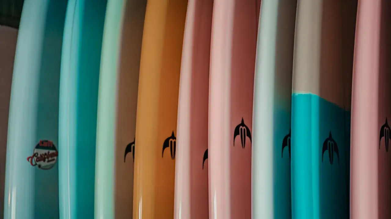 Reihe bunter Surfboards in Pastelltönen. Welches Surfboard passt zu mir? Die Auswahl ist groß, von hellblau bis rosa.