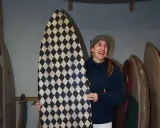 Frau lacht und hält ein selbstgebautes Surfbrett mit Rautenmuster.