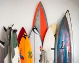 Eine Sammlung bunter Surfbretter steht an einer weißen Wand. Sie sind bereit für das nächste Abenteuer auf den Wellen beim Wellenreiten.
