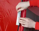 Hände flicken ein rotes Zelt mit silbernem Klebeband.