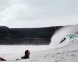 Surfer wartet auf die perfekte Welle vor der Felsküste. Windsurfen Fuerteventura.