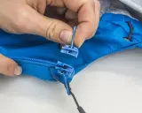 Hände tauschen den blauen Reißverschluss-Zipper an einer Jacke aus.