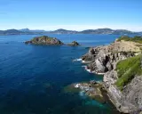 Felsige Küste der Halbinsel Giens mit türkisfarbenem Wasser und grüner Vegetation. Im Hintergrund die Silhouette der Küste.