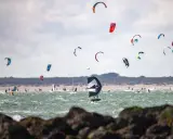 Viele bunte Kites und Surfer bevölkern das Meer am Brouwersdam Zeeland. Ein Kitefoiler schwebt über dem Wasser.