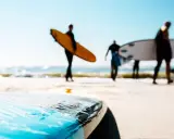 Surfer in Holland tragen ihre Boards zum Wasser. Die Sonne scheint, die Wellen brechen.