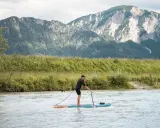 Mann auf SUP-Board, der geradeaus fährt, mit Bergen im Hintergrund.