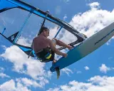 Ein Windsurfer mit einem Freeride Windsurfboard springt hoch in den blauen Himmel mit Wolken.