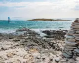 Ein Windsurfer gleitet über das türkisfarbene Meer vor Kroatien. Steinformationen säumen die felsige Küste.