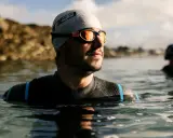 Mann mit Schwimmbrille und Badekappe im Wasser, bereit für das Schwimmen. Die Schwimmbrille reinigen ist wichtig für klare Sicht.