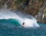 Surfer reitet eine grüne Welle vor einer felsigen Küste. Perfekt für die Surf-App, um die nächste Session zu planen.