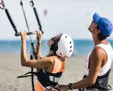 Frau und Mann bereiten sich auf das Surfen mit Drachen in der Hand vor. Sie stehen am Strand, das Meer im Hintergrund.