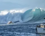 Sarah Hauser surft auf einer riesigen Welle, die sich hinter ihr bricht. Ein Boot mit der Aufschrift "Fiji S" liegt im Vordergrund.
