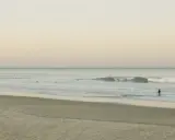 Ein Surfer geht ins Meer, um Cornwall zu surfen. Sanfte Wellen brechen am Strand.