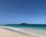 Kitesurfer tanzen über das türkisfarbene Wasser am Flag Beach Corralejo. Ein einsamer Schwimmer genießt die Sonne.