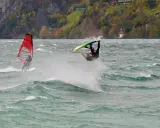 Windsurfer vollführt Sprung am Starnberger See. Ein weiterer Surfer mit rotem Segel im Hintergrund.
