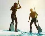 Ein Paar genießt das Stand-Up-Paddling (SUP) auf dem Meer. Sie stehen auf ihren Boards und halten Paddel, während die Sonne scheint.